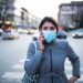 Woman with mask talking on the phone, she walking on crossroad in the city.